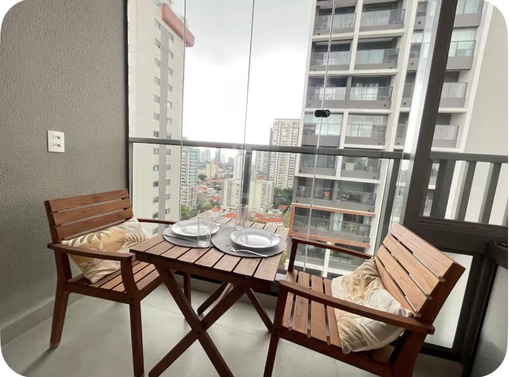 A balcony with a table and two wooden chairs, a view of tall buildings, and a railing.