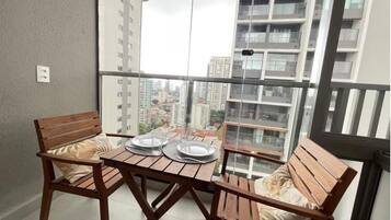 A balcony with a table and two wooden chairs, a view of tall buildings, and a railing.