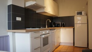 A compact kitchen with a stove, oven, microwave, and a coffee maker. - La Ferme Tranquille Gîte de Groupe (Puivert)