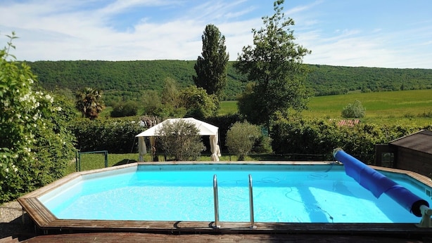 A rectangular swimming pool with a wooden deck, surrounded by lush greenery and hills in the background. - La Ferme Tranquille Gîte de Groupe (Puivert)