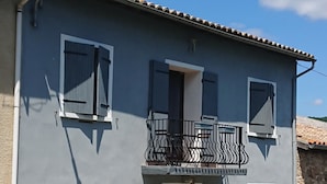 A two-story building with a balcony, a chimney, and a garden with pink flowers. - La Ferme Tranquille Gîte de Groupe (Puivert)