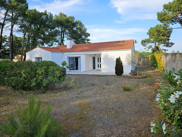Une maison blanche d’un seul étage, avec un toit recouvert de tuiles rouges, une terrasse couverte et une allée gravillonnée.