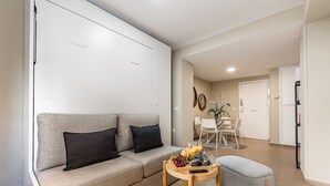 A modern living room with a grey sofa, a small wooden table with fruits and drinks, and a grey ottoman. - Waou Seville Center I (Sevilla)