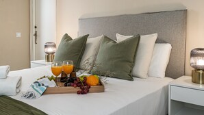 Un letto rifatto con cuscini, un vassoio con frutta e succo, e un comodino con una lampada.