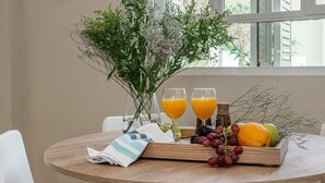 Un tavolo rotondo in legno con un vassoio di frutta, due bicchieri di succo d'arancia e un vaso con fiori.