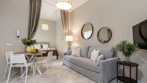 A modern living room with a grey sofa, white chairs, a round table, and a small side table with a plant. - Waou Seville Center III (Sevilla)