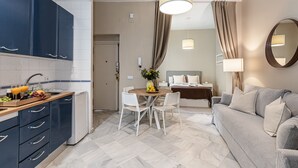 A modern hotel room with a kitchen area, a dining table with chairs, a sofa, and a bed. - Waou Seville Center III (Sevilla)