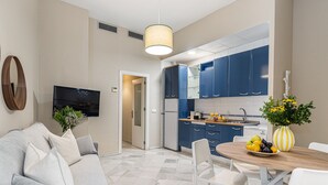 A modern kitchen with blue cabinets, a dining area with a table and chairs, and a living room with a sofa and a TV. - Waou Seville Center III (Sevilla)