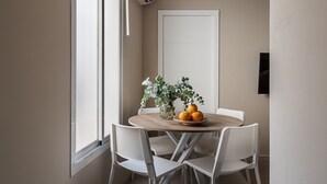Comedor con una mesa redonda, sillas blancas, un florero con follaje verde y dos naranjas sobre la mesa.
