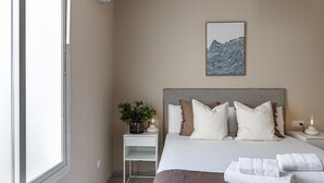 Un dormitorio con cama, mesita de noche, lámpara y una obra de arte en la pared.