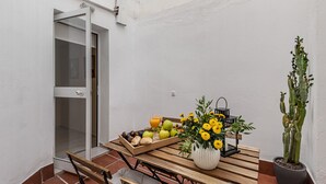 Una mesa de madera con un frutero, un florero con flores amarillas y un cactus en maceta.