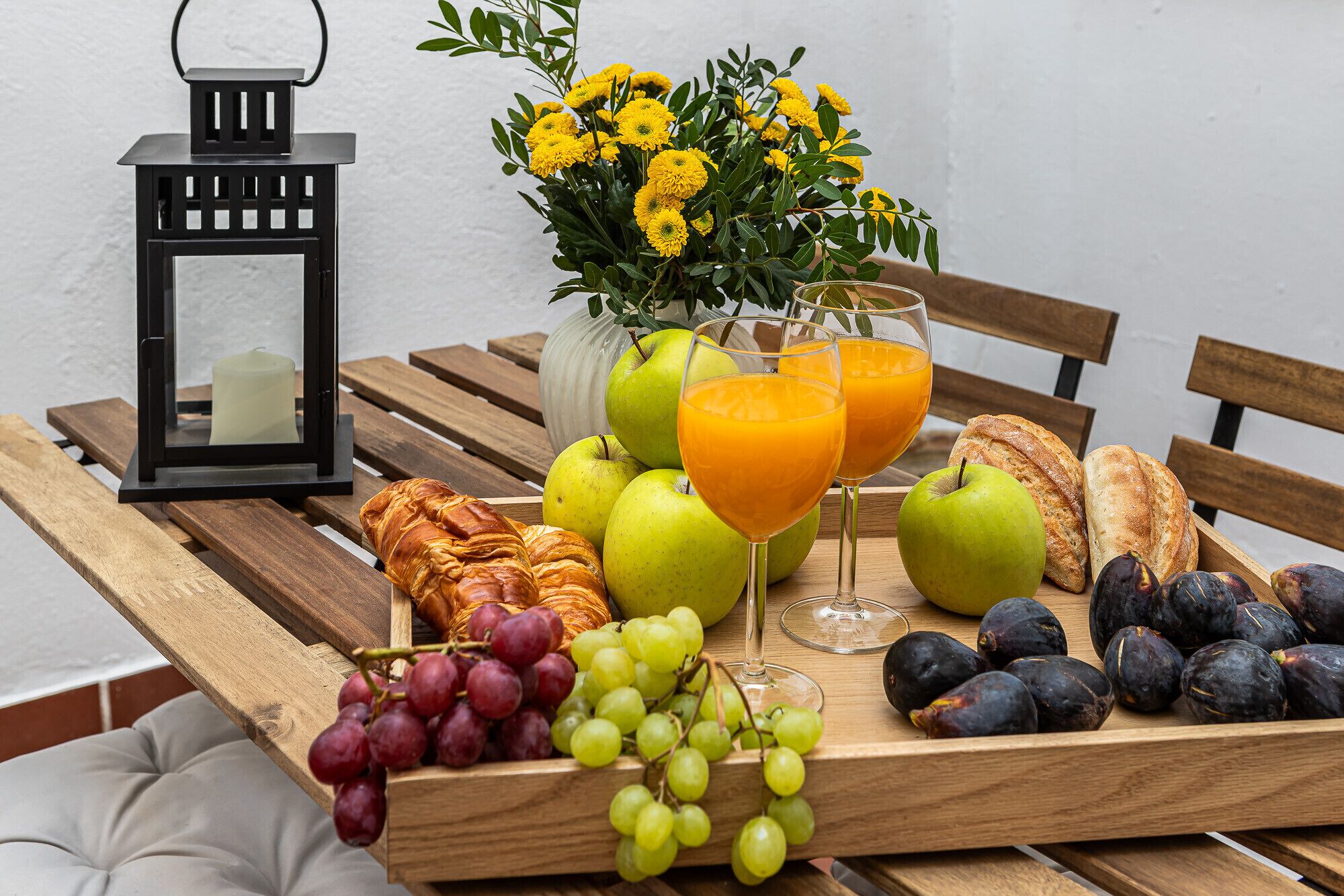 Un plateau en bois contenant des fruits, du pain et des boissons, posé sur un banc.