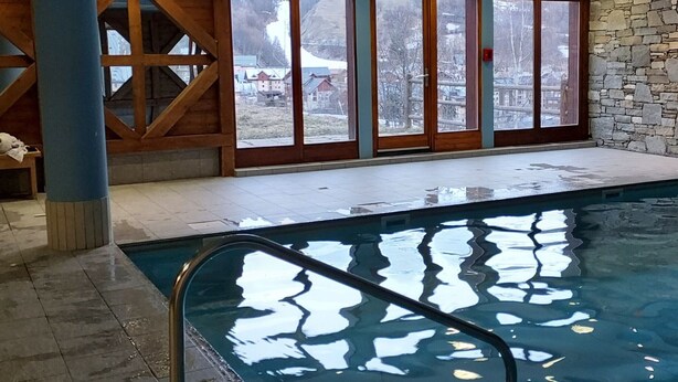 An indoor swimming pool with a view of a snowy landscape through large windows.