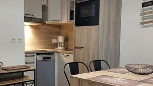 A compact kitchen with a dishwasher, a coffee maker, and a microwave. There is a dining table with chairs and a decorative bowl.