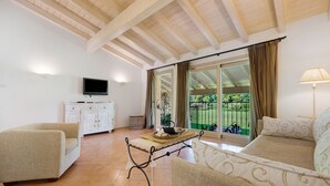 Una sala de estar con sofá, mesa, televisor y balcón con cortinas.