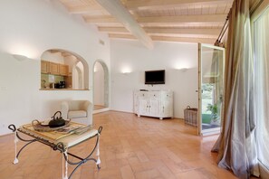 A spacious room with a wooden ceiling, a television mounted on the wall, a white cabinet, and a table with a basket and kettle.