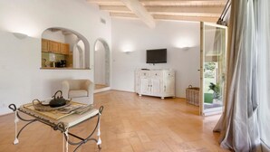 Una habitación amplia con techo de madera, televisor montado en la pared, un armario blanco y una mesa con una cesta.