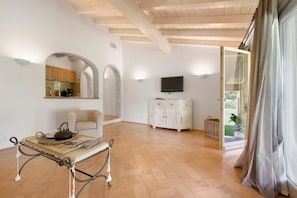 A spacious room with a wooden ceiling, a television mounted on the wall, a white cabinet, and a table with a basket.