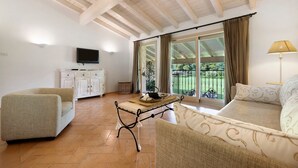 Una habitación con sofá, mesa, televisor y balcón con cortinas.