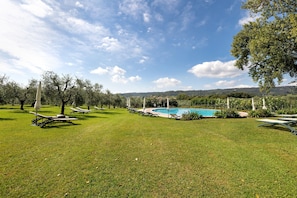A pool area with lounge chairs and tables, surrounded by grass and trees.