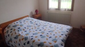 Un dormitorio con cama, mesita de noche, ventana y radiador.