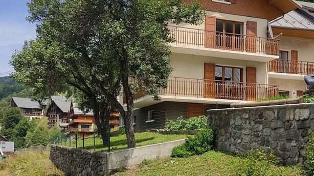 Un edificio de varios pisos con balcones, rodeado de vegetación y muros de piedra.