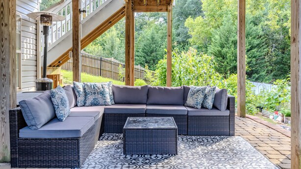 Een overdekt terras met een hoekbank en salontafel, omgeven door een houten pergola en uitzicht op een tuin en bomen.