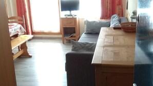 Ein gemütliches Zimmer mit Holztisch, Sofa, Bank und Fernseher auf einem Holzständer.