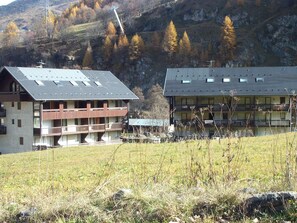 A building with multiple balconies and a flat roof, surrounded by a grassy field and mountains in the background. - 2P Cabin 4 Pers, Pets Allowed, Balcony, Parking (Valloire)