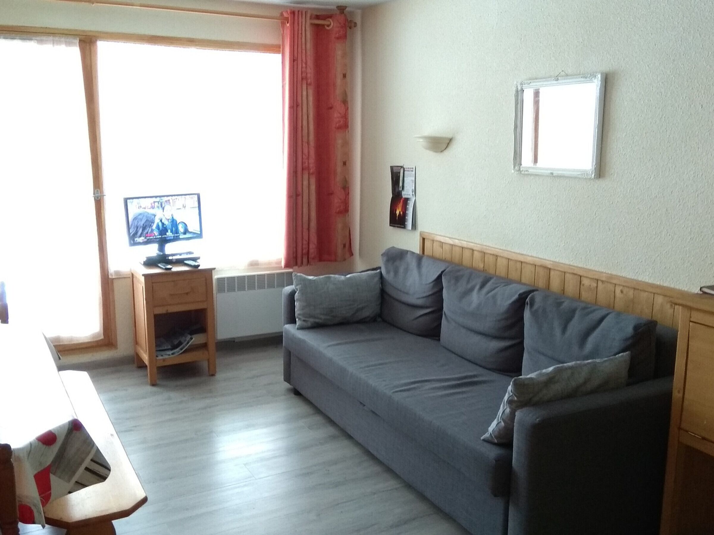 A living room with a grey sofa, wooden sideboard, and a television on a wooden stand.