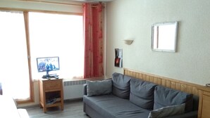 Ein Wohnzimmer mit grauem Sofa, einer Holzkommode und einem Fernseher auf einem Holztisch.