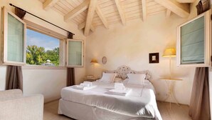 A bedroom with a bed, two bedside tables, a lamp, a window, and a view of trees.