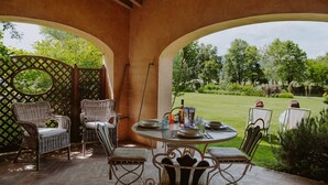 An outdoor patio with wicker furniture, a round table set for dining, and a view of a well-maintained garden.