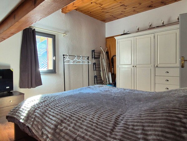 A bedroom with a bed, a wardrobe, a window with curtains, and a drying rack.