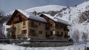 A multi-story chalet with balconies, surrounded by snow-covered hills.