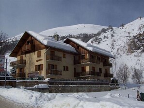 A multi-story chalet with balconies, surrounded by snow-covered hills.