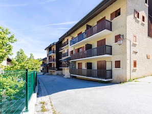 A multi-story building with balconies, a green fence, and a clear sky.