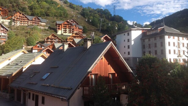 A mountainous village with traditional wooden houses and a large white building, likely a hotel, with a view of the surrounding hills.