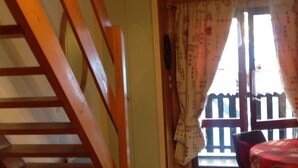 A room with a wooden staircase, a balcony with a railing, and a table with a red tablecloth.