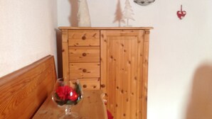 A wooden cabinet with drawers, a glass vase with red flowers, and a small white Christmas tree on top.