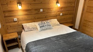 A wooden-paneled bedroom with a bed, two bedside tables, and wall-mounted lights. - Chalet for 8 facing south, terrace, private parking (Valloire)