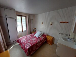 Quarto com cama, mesa de cabeceira e banheiro com pia.