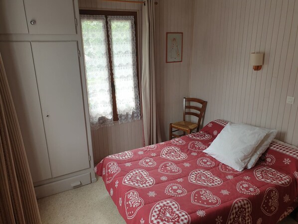Une chambre à coucher avec un lit, une chaise, une armoire et une fenêtre avec des rideaux.