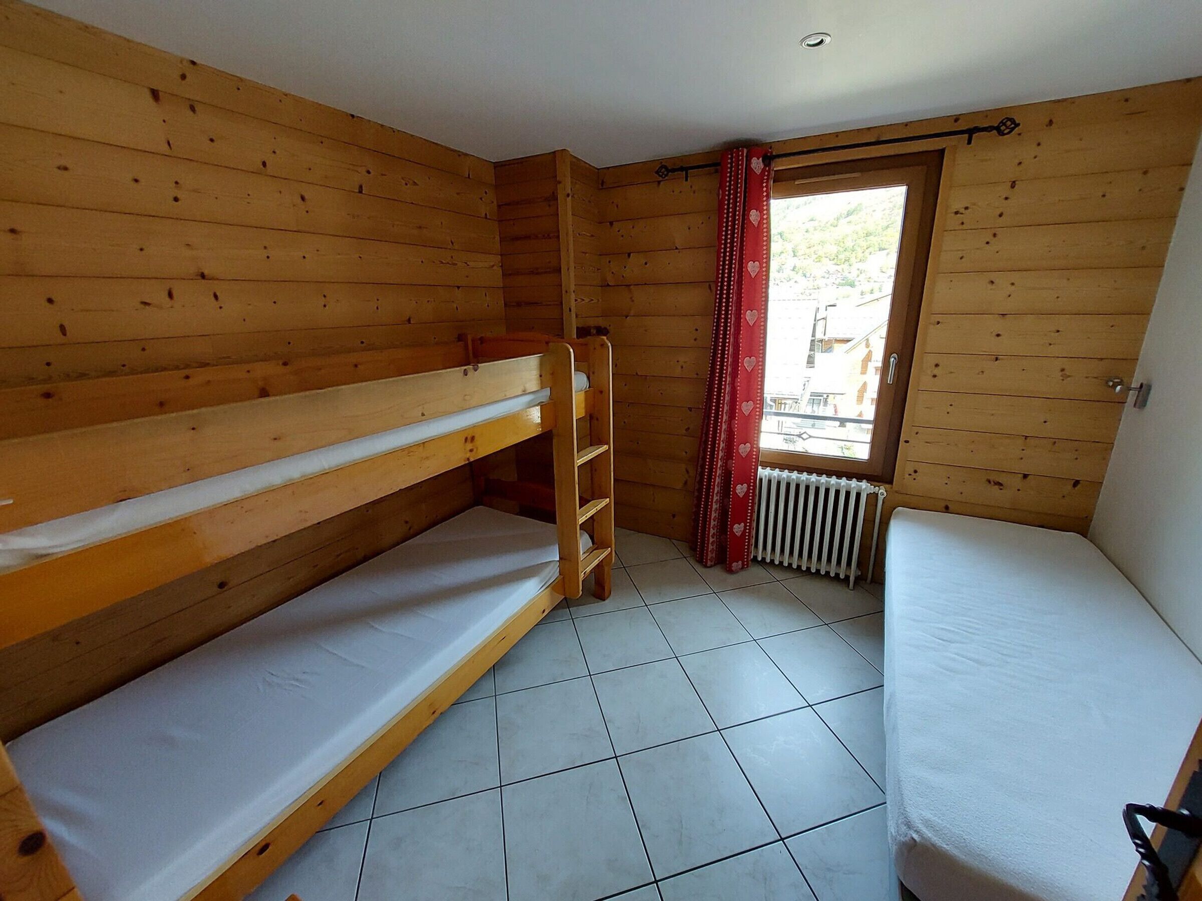 Una habitación pequeña de madera con literas, una ventana con cortinas rojas y un radiador.