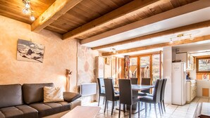 A cozy living area with a sofa, a coffee table, and a dining table with chairs. There is a stone wall and a wooden ceiling. - 3* Apartment for 8 people, pets allowed, parking (Valloire)