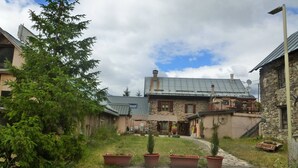 A rustic building with a stone facade, a metal roof, and a wooden deck. There are potted plants in front of the building. - 3* Apartment for 8 people, pets allowed, parking (Valloire)