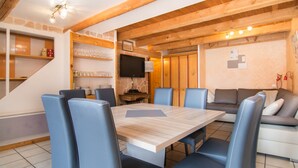 A dining area with a wooden table and blue chairs, a sofa, and a TV on the wall. - 3* Apartment for 8 people, pets allowed, parking (Valloire)