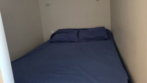 Habitación pequeña con cama individual, colcha azul oscuro y dos interruptores de luz blancos en la pared.
