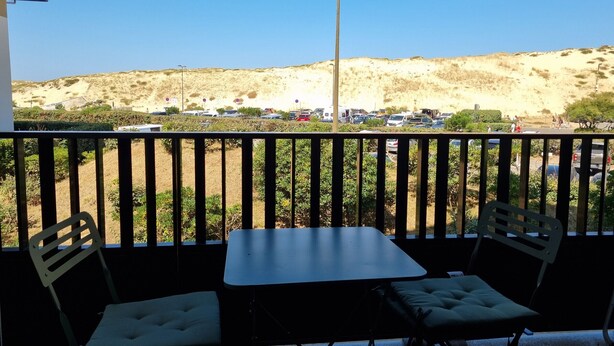 Un balcón con una mesa y dos sillas, con vista a un estacionamiento y un paisaje montañoso.