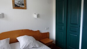 Habitación de hotel con cama, almohadas, mesita de noche, lámpara de pared, cuadro enmarcado y una puerta color turquesa.
